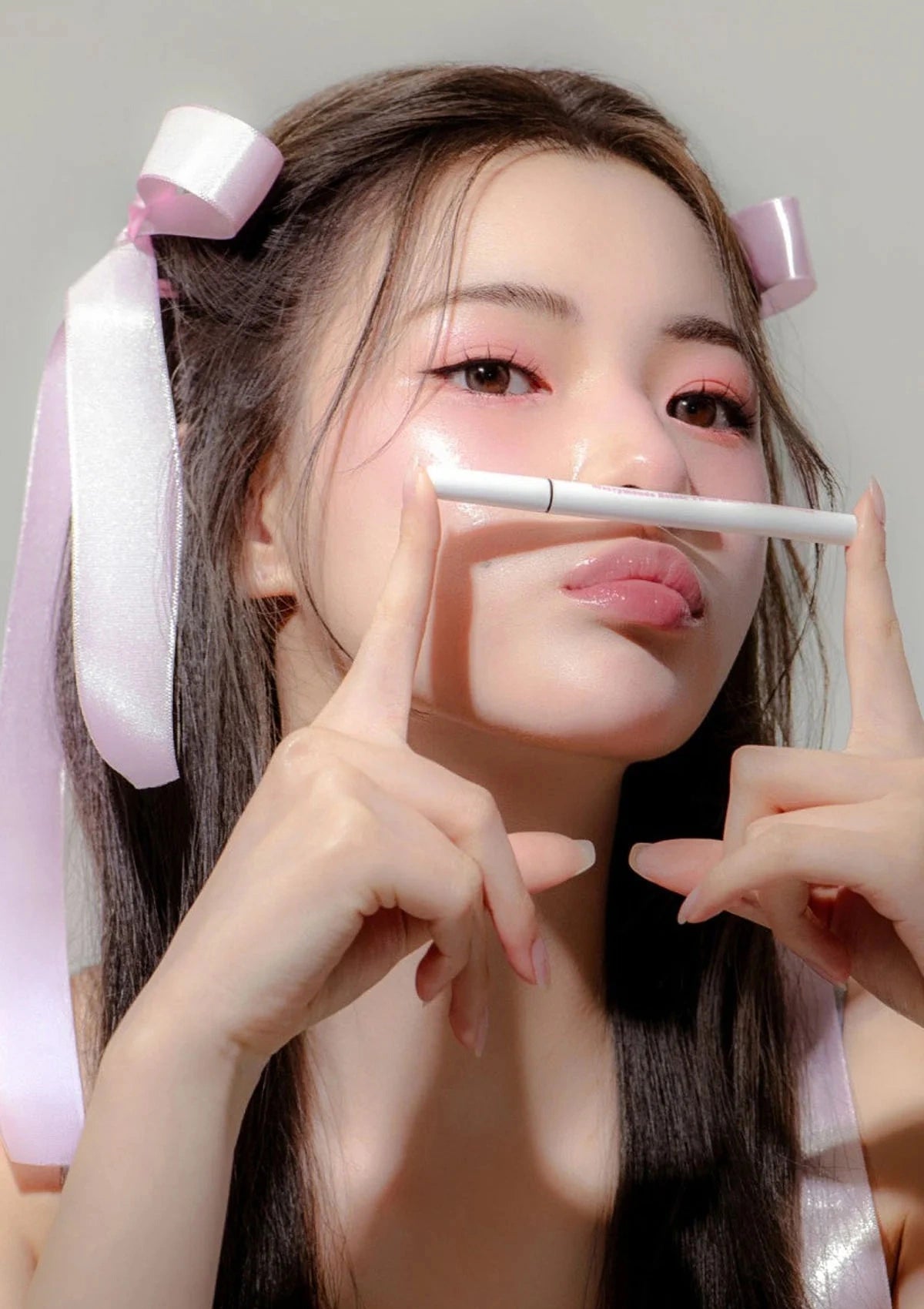 Person with pink ribbons in hair holding a makeup brush near face